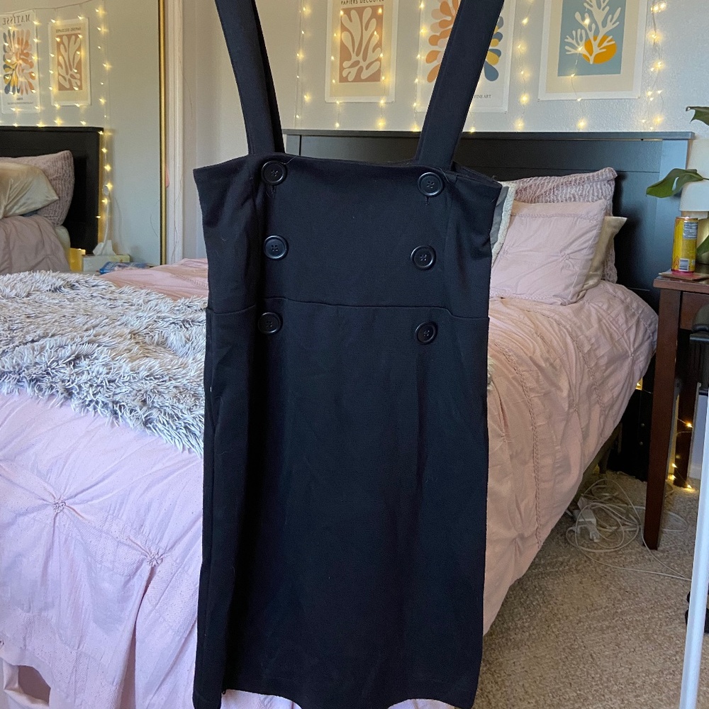 Black overall dress with long straps and 6 buttons at the waist